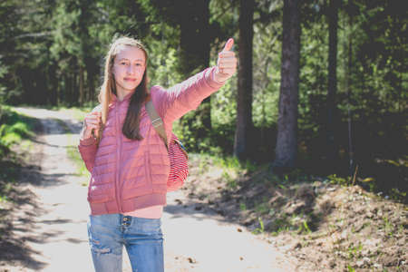 One cheerful brown-haired traveler teen girl, showing thumb up.Close up of teenager hand gesturing thumbs up in a park Spending spare time in wild wood.Summer sunny day.の写真素材
