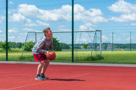 Boy preparing for basketball shooting at playground.Boy performs shot at basketball game on the playground during sunny summer day.の写真素材