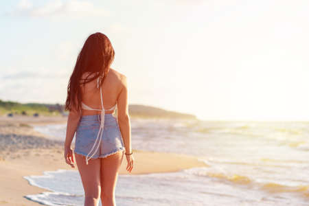 Lonely young woman walking on the beachsunset day.Beach woman in fashion beachwear relaxing walking near ocean water on summer vacation travel.Back view.の写真素材