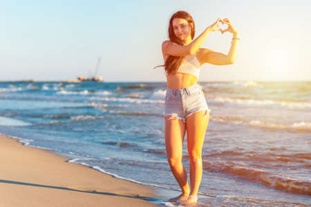Young woman making heart symbol with hands sun blue sky background.Beautiful girl showing heart sign by hands at summer sunny day or evening outdoor.の写真素材