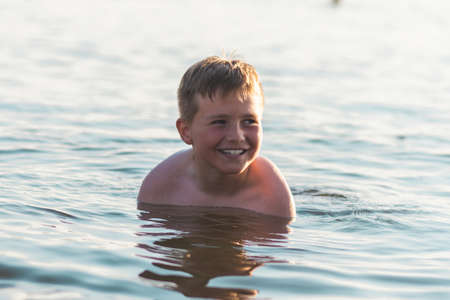 Cute young boy enjoy having fun at lake or beach water on warm sunset evening time outdoors.Happy childhood vacation at countryside concepton.Boy at pier warm summer day having good time in a water.の写真素材