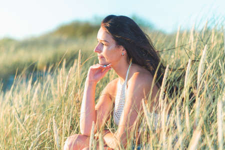 Portrait of a beautiful young woman on meadow watching the sunset enjoying nature summer evening outdoors.Beautiful young woman lies or sitting on the grassの写真素材