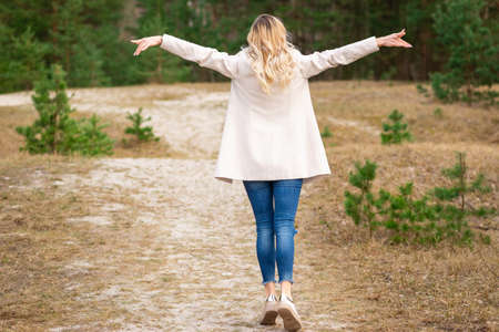 One young beautiful blonde long haired woman standing backwards and raised hands over green...
