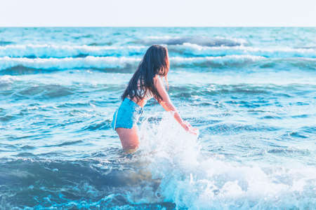 Young woman playing in the sea in summer. woman make in sea water splash.Cheerful young woman having fun on the beach. She is splashing in the sea water and enjoys on vacation.の写真素材