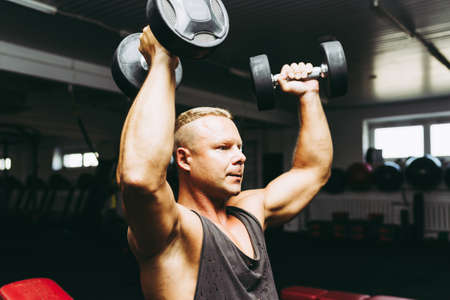 Young fit man in a gym exercising with dumbbells.healthy man working out with dumbbells.Copy space.closeup.Toned.の写真素材