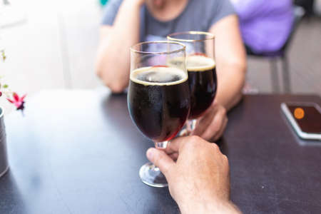 Woman and man drink beer. Friends met in a pub. Two glasses of dark beer.Two people toasting with...
