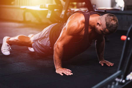 Sport young athletic man doing push-up. Muscular and strong guy exercising at a gym.Strength and motivation concept.Young handsome man in sportswear doing push ups at gym.Selective focus.Toned.の写真素材