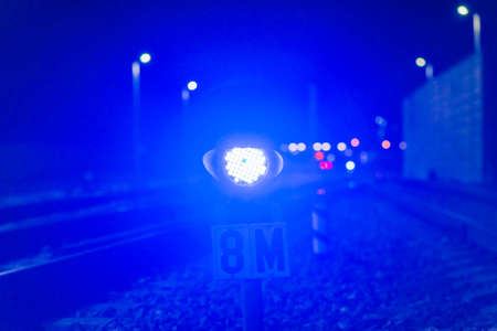 The blue traffic light at the night railway station glows blue. In the distance, haze and glowing lanterns. near the railway.Blurred background.の写真素材