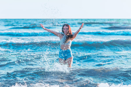 Young woman playing in the sea in summer. woman make in sea water splash.Cheerful young woman having fun on the beach. She is splashing in the sea water and enjoys on vacation.の写真素材
