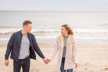 Attractive young couple walking along the shore of a sandy beach, on a spring romantic holiday, outdoors. Travel tourists lifestyle. Couple enjoying loving time together.の写真素材