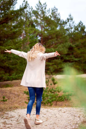One young beautiful blonde long haired woman standing backwards and raised hands over green background outdoor. Young woman arms raised enjoying fresh air in a forest.Freedom happiness concept.の写真素材