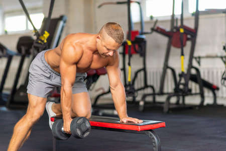 Strongman bodybuilder exercising with dumbbell in a gym.Young handsome adult male doing one arm dumbbell rows on bench in modern gym.Copy space.の写真素材