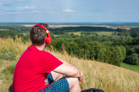 Young male person enjoys music in headset from cell phone in mountains.beautiful scenery male listening to music on the mountain.Summer evening.Back viewの写真素材