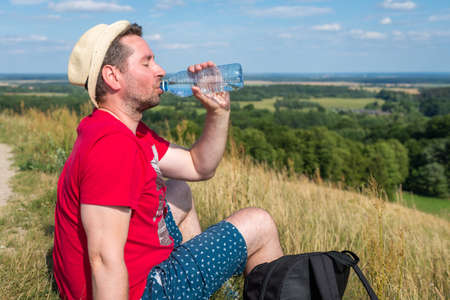 Traveler drinks water in the mountains.Hiker with backpack relaxing on top of the mountain and drinking bottled water in summer sunny day.の写真素材