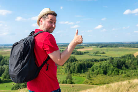 Cheerful travel man showing thumb up. traveler with straw hat showing thumb up against beautiful summer valley.Travel and nature explore concept. Copy space.の写真素材