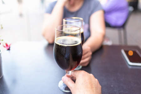 Woman and man drink beer. Friends met in a pub. Two glasses of dark beer.Two people toasting with glasses goblets glasses of beer.の写真素材