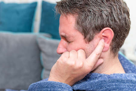 Middle age caucasian man wearing bathrobe covering ear with fingers. Pain concept.Side view.Closeup.の写真素材