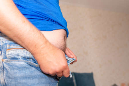 A middle aged slightly over weight man, trying to put on a pair of jeans.Man putting on weight and...