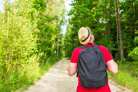 Traveler young man walking on path in the summer forest.Back view of young man with backpack traveling alone forest on warm summer day.Tourism and active lifestyle concept.の写真素材