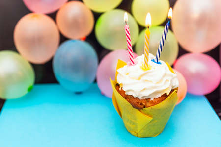 Birthday cupcake.Pastel yellow birthday cupcake with candle and blurred balloons.colorful birthday cupcake with a colored candle.Closeup,copy space.Birthday concept.の写真素材