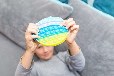 Schoolboy 10s boy lying on the couch and playing with sensory fidget toy at home. Kid plays stress and anxiety relief fidgeting game after learning.の写真素材