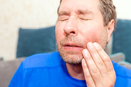 Toothache. Frustrated young man touching his cheek. middle age man is touching his cheek by his hand, he has a pain of teeth, toothache.Man sitting at home.の写真素材