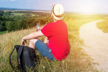 Traveler drinks water in the mountains.Hiker with backpack relaxing on top of the mountain and drinking bottled water in summer sunny day.の写真素材