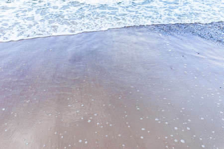 Soft wave of the sea on sandy beach white foam.Top view of a wave breaking on the sand at the...