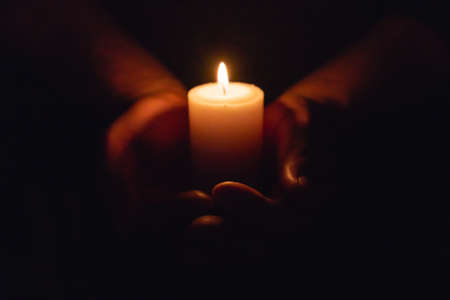 Hands holding burning candle in dark like a heart.Selective focus,black background.の写真素材