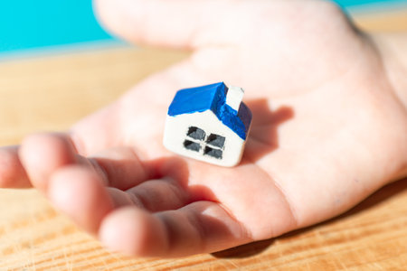 Small white toy house in the one hand of a young boy,selective focus,blurred wooden background.