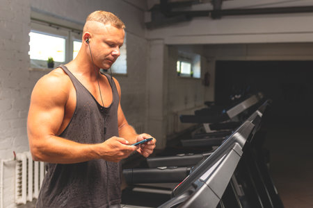 Man in gym using smartphone with headphones sportsman in headphones choose music on his smartphone, preparing for workout at gym. Modern technologies, healthy lifestyle concept.Copy space.の写真素材
