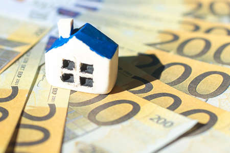 Miniature toy house placed on Euro bill banknotes. Concept for real estate costs, prices, buy or rent a house, hypothecary credit, interest.Selective focus,closeup.Blurred background and foreground.の写真素材