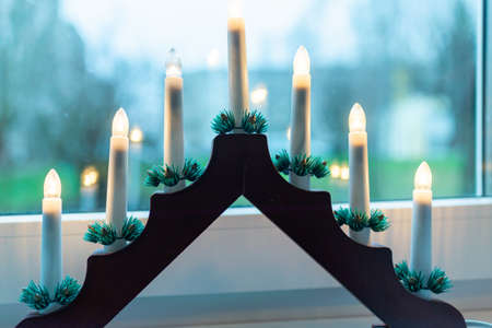 Advent electric candles on window sill.electrical advent candles by the window with urban blurred city buildings view.の写真素材