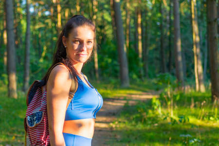 Young woman traveler with backpack walking in a summer forest, wanderlust travel concept,copy space.