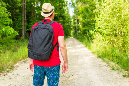 Traveler young man walking on path in the summer forest.Back view of young man with backpack traveling alone forest on warm summer day.Tourism and active lifestyle concept.の写真素材
