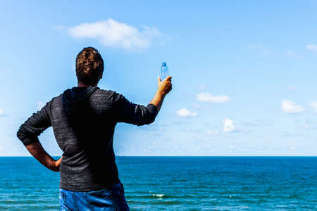 Middle age man relaxing and holding water bottle on the beach after promenade at summer sunny day.Copy space.の写真素材