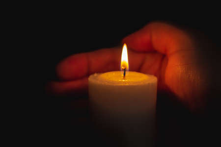 One palm take care of candle fire at night.Selective focus,Dark black background.Closeup.の写真素材