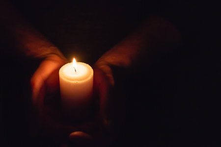Hands holding burning candle in dark like a heart.Selective focus,black background.Copy space.の写真素材