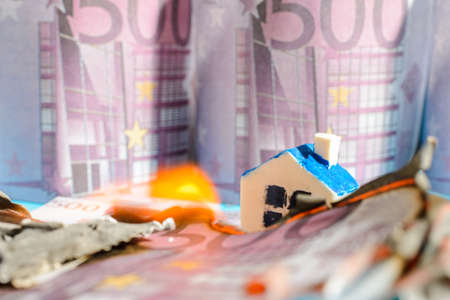 Miniature toy house fire burning Euro bill banknotes.close up.Blurred long exposure background and foreground.Indoors shot.の写真素材
