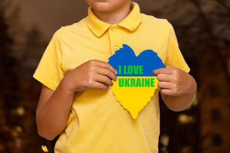 Inscription I LOVE UKRAINE.Boy holding flag of Ukraine with the heart shape symbol.the city background is blurry.Selective focus.の写真素材