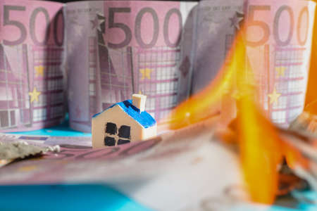 Miniature toy house fire burning Euro bill banknotes.close up.Blurred long exposure background and foreground.Indoors shot.の写真素材