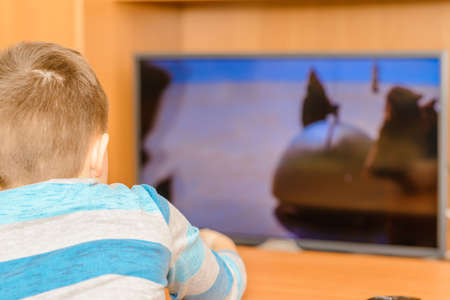 Young boy watching movie and holding remote control near TV screen at home.Selective focus,back view image.の写真素材