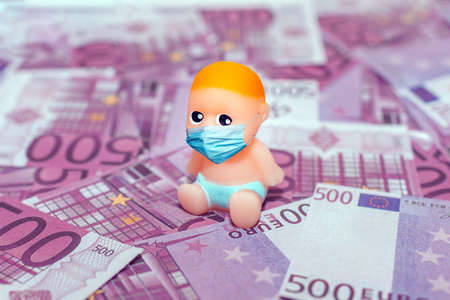 miniature toy newborn baby wearing a face mask,sitting on a pile paper cash 500 money background....