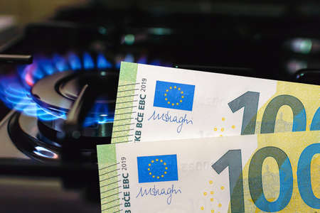 Gas burning flame 100 euro banknotes near gas stove at home.Gas flame with blue...