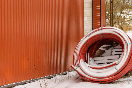 Coiled red plastic pipes stored winter outdoors near orange,background,selective focus,copy space.