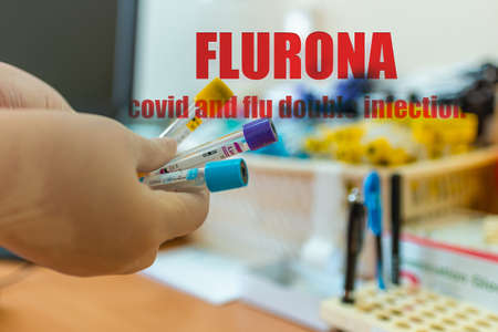 Inscription Flurona covid and flu double infection Coronavirus.Covid-19 and flu. Text and lab or laboratory.Scientist holds tube blood sample vacuum flask.Selective focus.の写真素材