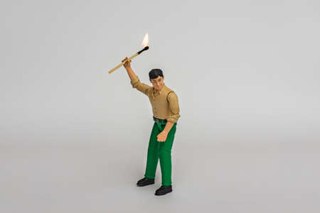 Miniature toy businessman figure holding burning mach stick, on white gray background.の写真素材