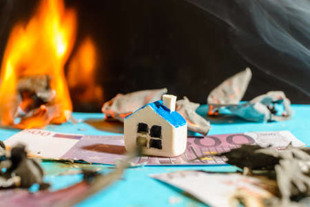 Miniature toy house fire burning Euro bill banknotes.close up.Blurred long exposure background and foreground.Indoors shot.の写真素材