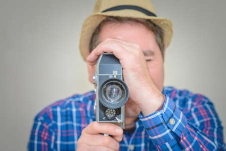 Man with Camera.cameraman make film on a retro camera.man with a plaid shirt filming with a Super 8 camera indoors.Closeup,toned,selective focus.Gray background.の写真素材