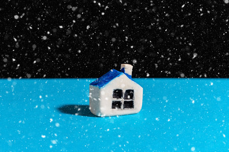 Miniature toy house stand on the blue snowing black background.Indoors shot.Home insurance concept.Copy space.の写真素材